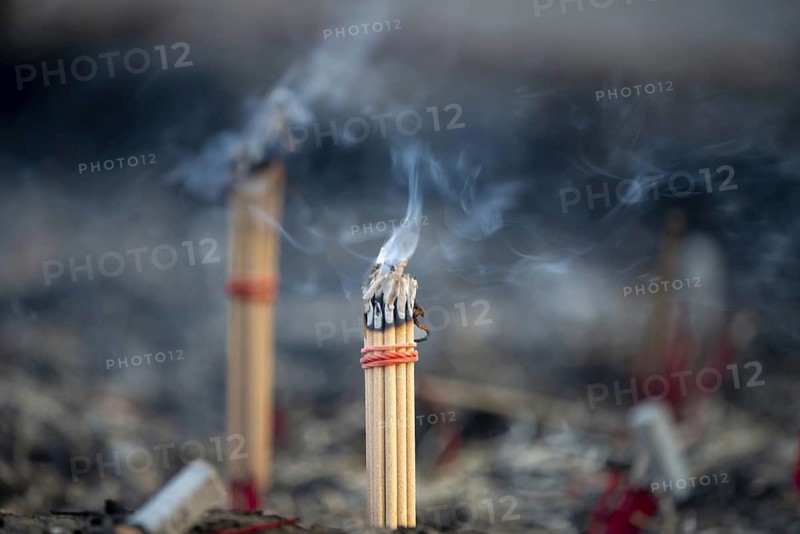 Fine smoke rises between the upright incense sticks and forms soft, swirling lines in the warm air. The bundles are carefully tied and depict a serene scene of traditional offerings such as those found in many temples and shrines, Wat Yai Chai Mongkon, Ayutthaya, Thailand