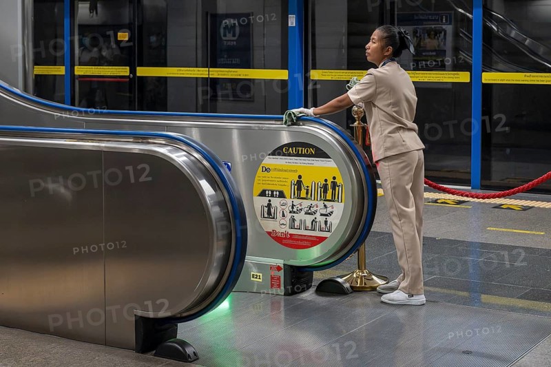Woman cleaning escalator handrail, Bangkok, Thailand