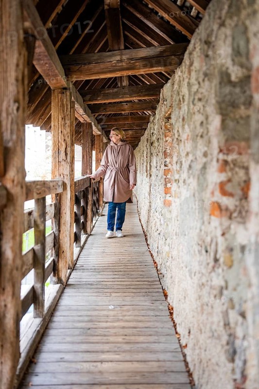 Woman walking in a long wooden tunnel next to a stone wall in a quiet medieval atmosphere, Isny, Allgäu, Bavaria, Germany