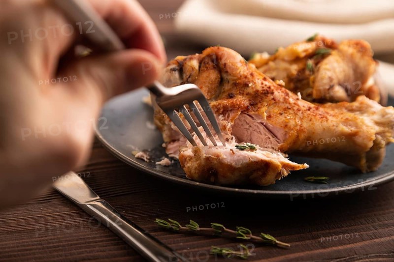 Fried Turkey Wing with spices and thyme on plate with hand on brown wooden background and linen textile. side view, close up, selective focus