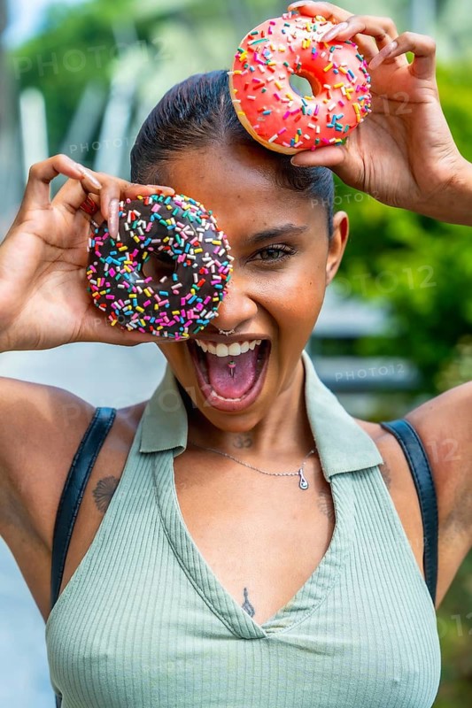 Joyful young woman with dark skin enjoying sweet donuts, holding them playfully over her eyes, expressing happiness and a carefree lifestyle
