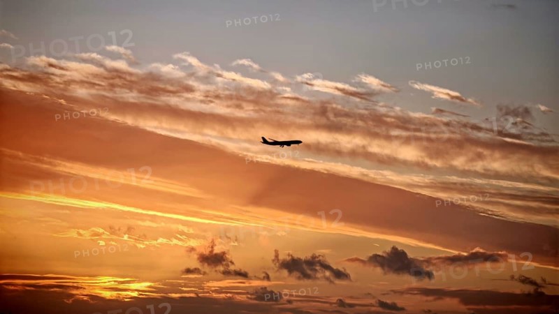 An airplane flies through a dramatically colored sunset sky, Lisbon, Portugal, Miradouro da Senhora do Monte McMlxii viewpoint, Lisbon, Portugal
