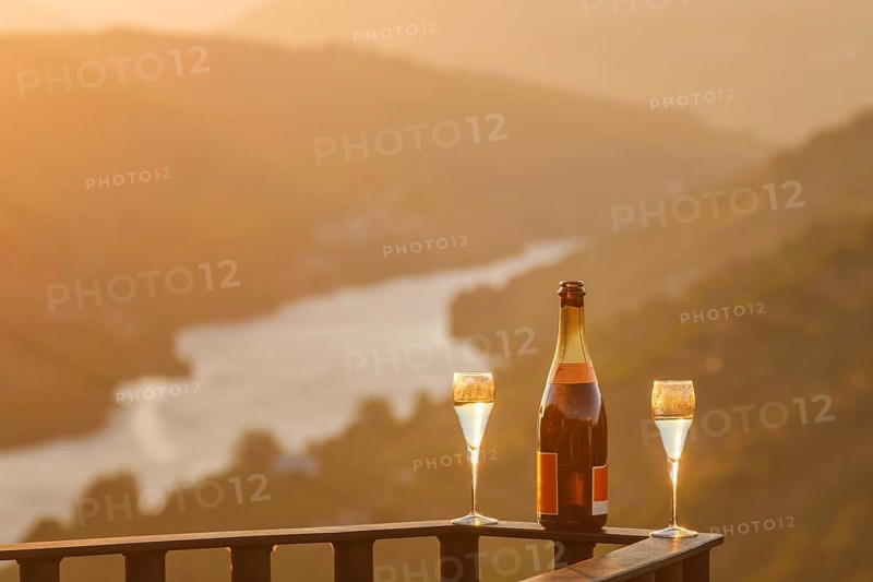 Bottle of sparkling wine and two glasses on a terrace railing with the Douro River glowing in soft morning light in the Douro Valley, Portugal
