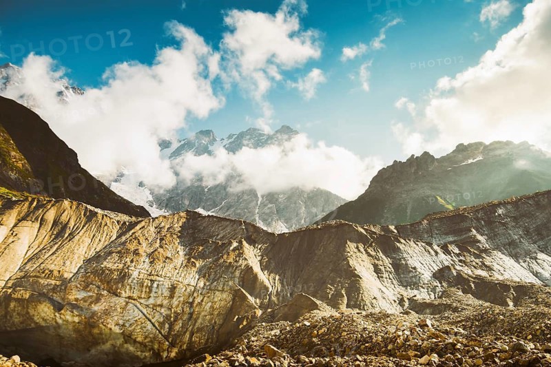 Georgia Svaneti Shkhara glacier summer morning with clouds drift across rugged peaks, moraine rocks foreground .Smoky mountains concept