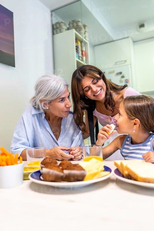 Grandmother, daughter, and granddaughter enjoying a joyful breakfast together in a bright kitchen, sharing food and connecting, representing family love and generational bonds