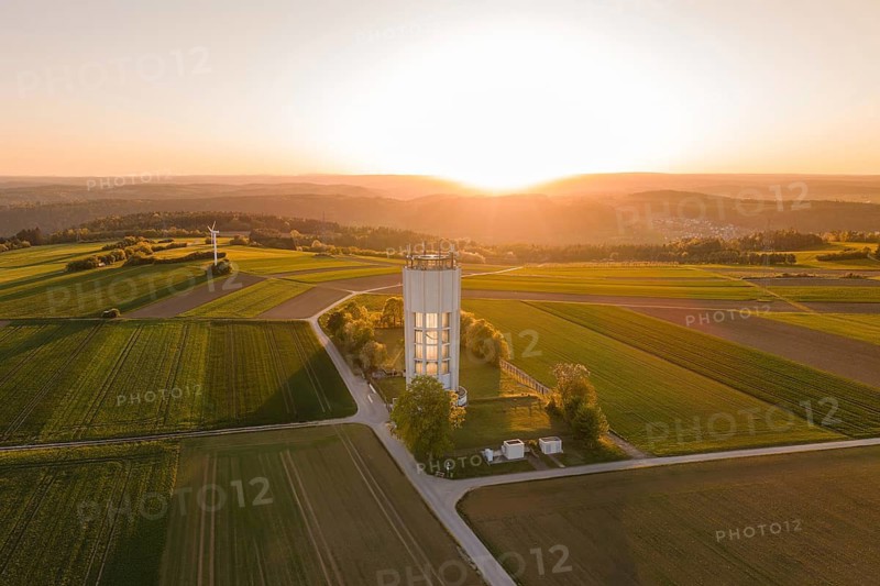 Sunset over fields with water tower and wind turbine, peaceful and wide landscape in warm light, Jettingen, Germany