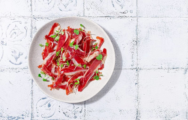 Ham of duck breast, dried duck fillet, with microgreens, plate, on a tiled table