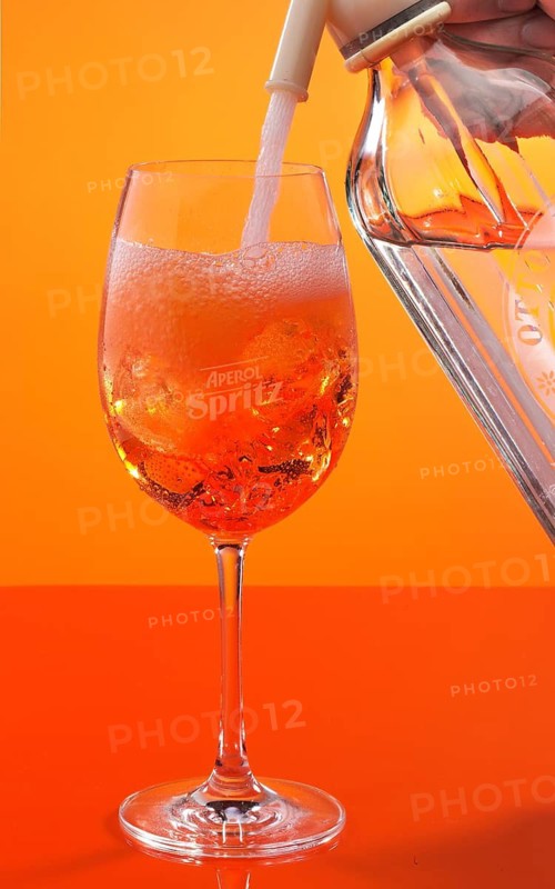 Aperol Spritz against an orange background is topped up with soda water