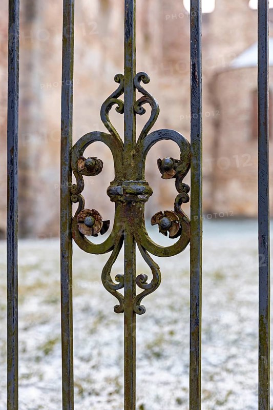 Close-up of an ornate, rusty iron fence on a cold winter day with snow-covered ground, iron grid at the abbey ruins in Bad Hersfeld