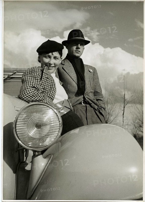 Fashion, vintage car, eagle, car, radiator figure, elegant woman, man, advertising photo, a smiling couple leaning against a car under a cloudy sky, Karl Theodor Gremmler, around 1935