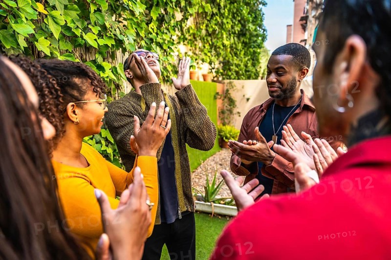 Diverse adults forming a support circle, clapping for one individual, expressing community, empathy, and mental wellness during an outdoor group therapy session