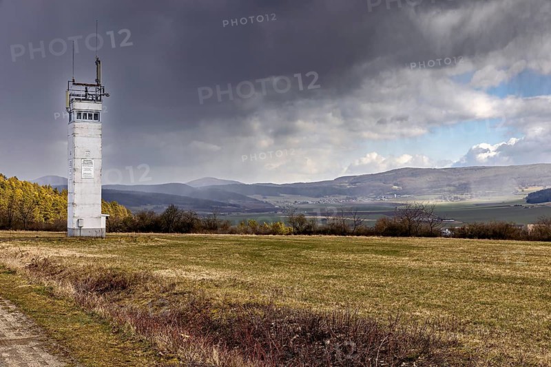 A watchtower stands in a vast, grassy landscape under dramatic clouds, The Point Alpha memorial between Rasdorf and Geisa in the Rhön