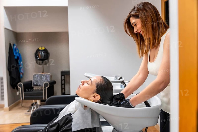 Hairdresser wearing gloves washes client's hair at a salon basin, providing professional shampoo and relaxing pampering treatment in a modern interior for comfort and care