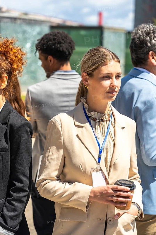 Young business professional attending an outdoor corporate conference, holding a coffee cup and wearing a name tag, ready for business networking and casual conversation during a break