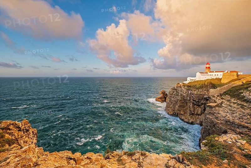 View of the Lighthouse of Cabo de Sao Vicente in Sagres, Algarve, Portugal, at sunrise with Atlantic ocean, cliffs, and dramatic clouds and sea