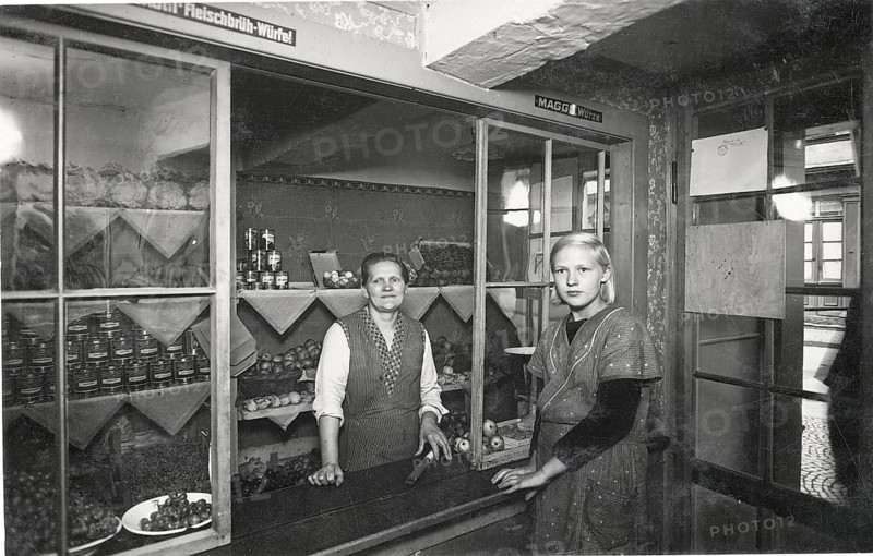Shop counter, colonial goods, village shop, fruit, vegetables, sale, shop, business, profession, twenties, saleswoman, poverty, two woman standing behind a counter in a small grocery store with shelves in the background, around 1928