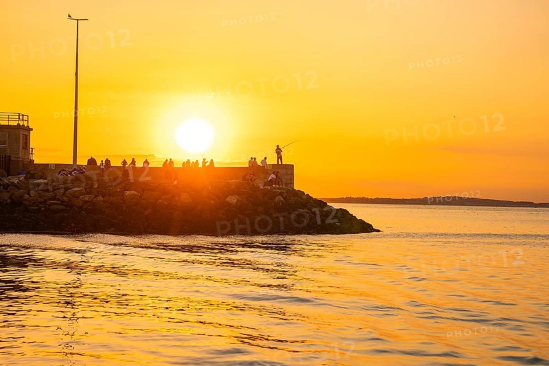 Sunset on the coast with people on a stone wall, warm and peaceful atmosphere, Howth, Ireland