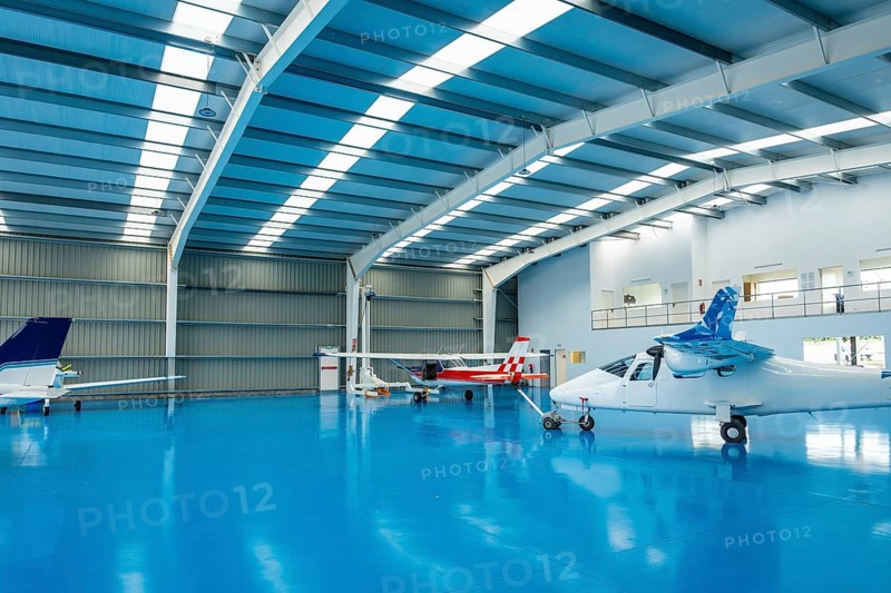 Modern aviation hangar featuring several small private light aircraft parked on a clean blue epoxy floor, representing business, transport, and luxury in private flying