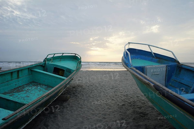 Two fishing boats, turquoise, rest on the beach as the sun gently illuminates the sky and touches the ocean, Ecuador