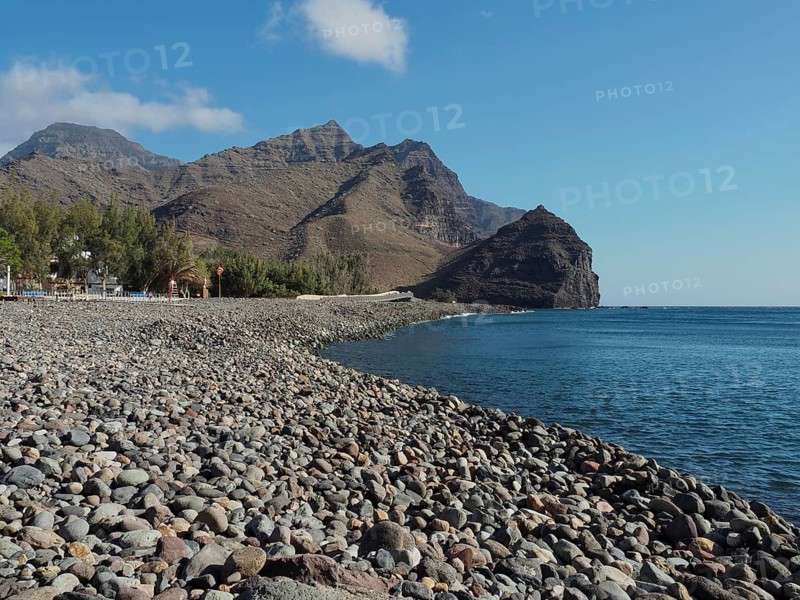 Pebble beach by the sea with mountains in the background on a sunny day, La Aldea de San Nicolas beach, Gran Canaria, Spain