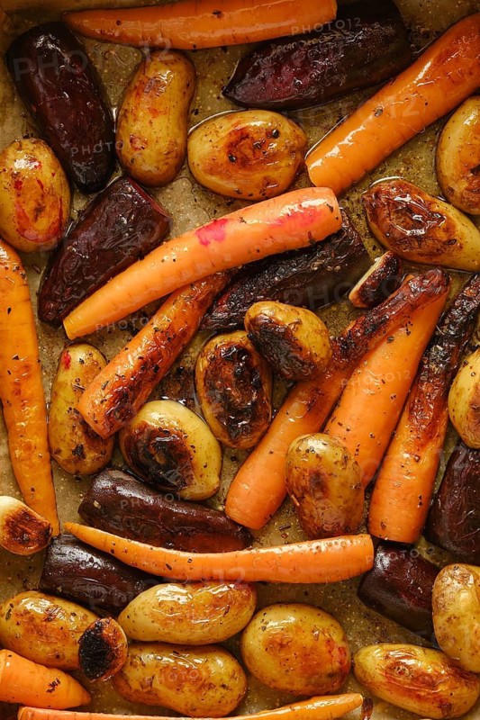 Colourful mix of roasted carrots, potatoes, and beetroot on baking tray. Fresh vegetables cooked until tender. Scene shows kitchen preparation for meal. Ideal for healthy eating options