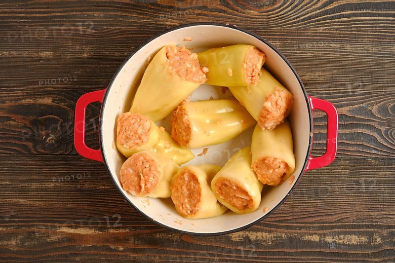Top view of bell peppers filled with meat and rice in red cast-iron pot on wooden table. This dish is ready to be cooked