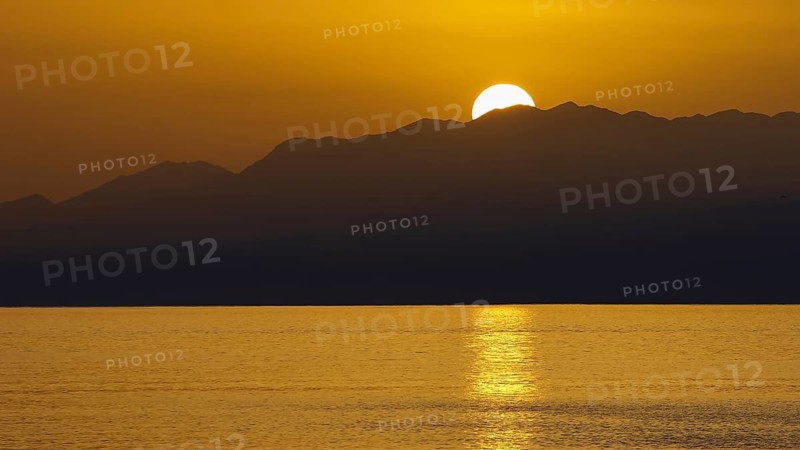 The sun sets behind the mountains and illuminates the sea golden, Matala, South Coast, Crete, Greek Islands, Greece