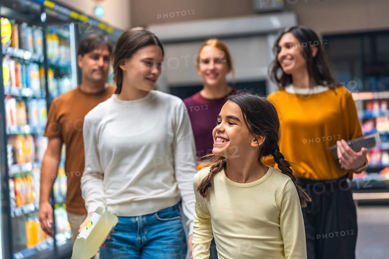 Happy family of five walking down supermarket aisle, smiling and choosing products from refrigerator shelves, enjoying daily grocery shopping experience