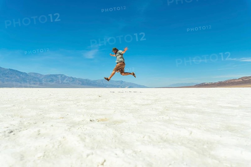 Man jumping joyfully across vast white salt flats of badwater basin, death valley, silhouetted against a clear blue sky, celebrating freedom, adventure and outdoor energy