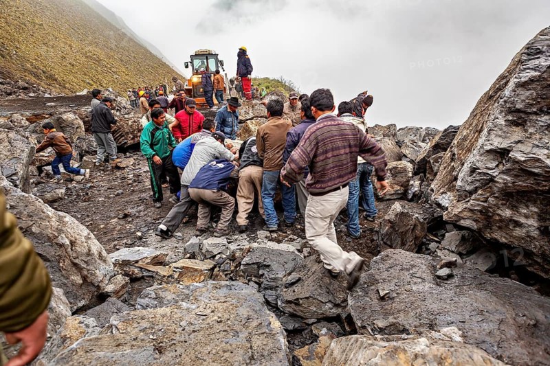 Group of people move a rock on a foggy mountain road with a tractor in the background, rockslide on the pass road towards Rurrenabaque through the Andes on the Road of Death in Bolivia