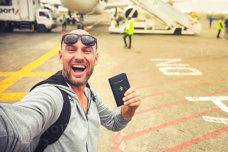 Excited young man traveler taking selfie airplane tarmac holding passport travel document departure airport terminal vacation journey flight boarding tourism holiday exploration transportation