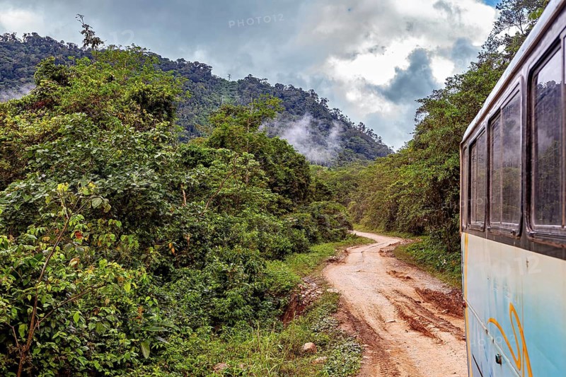 A bus travels along a dirt road surrounded by misty rainforest mountains, bus ride from La Paz towards Rurrenabaque through the rainforest on the Road of Death in Bolivia