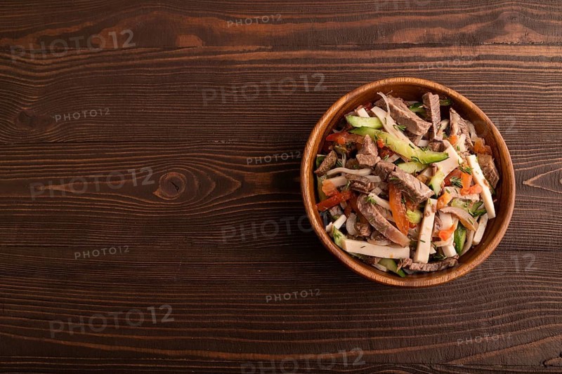 Meat salad with beef and vegetables in wooden bowl on brown wooden background. top view, flat lay, copy space