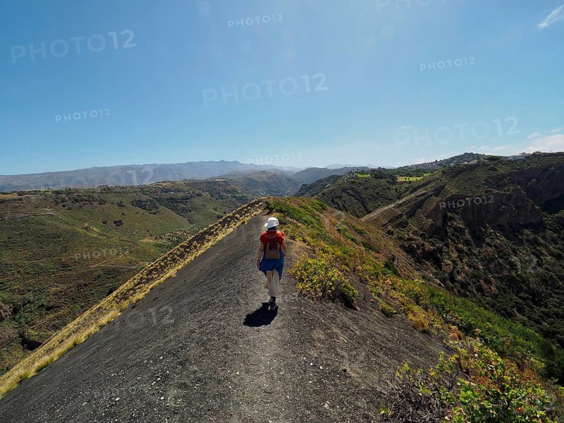 Person hiking on a narrow ridge with a view of a volcanic crater, Caldera de Bandama Natural Park, Gran Canaria, Spain