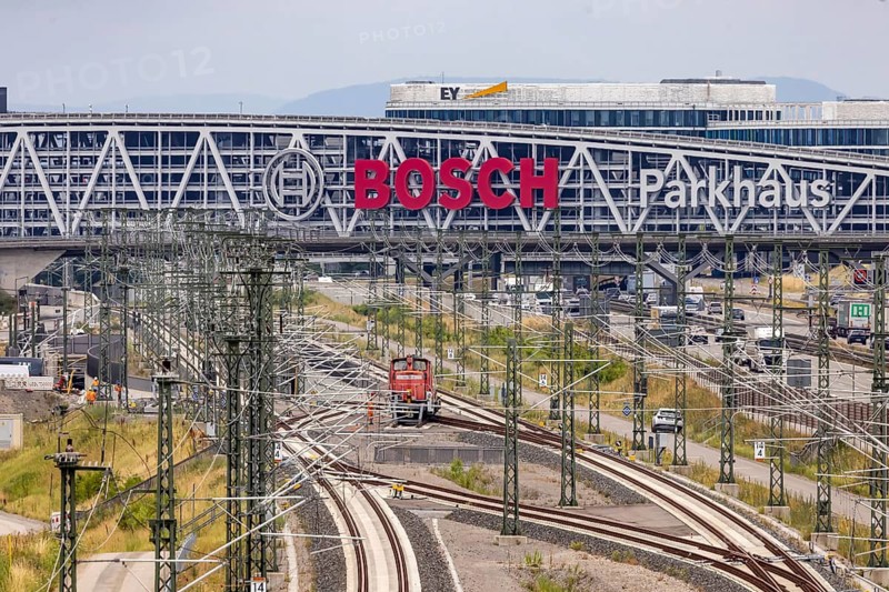 A8 motorway at Stuttgart airport with Bosch parking garage and new Deutsche Bahn AG line with locomotive. The 440 meter long construction offers space for 4200 vehicles. Bosch has the naming rights, the stylized ignition anchor measures 12 meters in diameter. This makes it one of the biggest neon signs in the world. Stuttgart, Baden-Württemberg, Germany