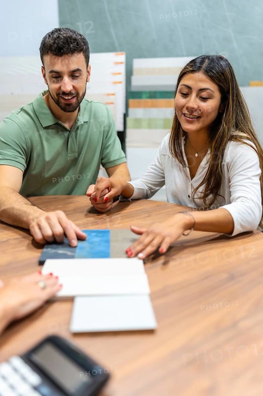 Young couple sitting at a table in a showroom, discussing and selecting different tile and flooring samples with an unseen salesperson for their new interior design or home improvement plans