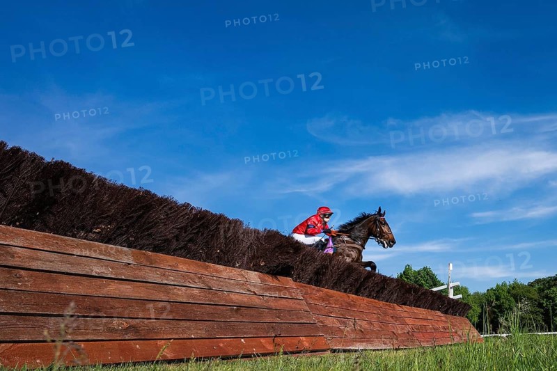 WROCLAW, POLAND - MAY 10, 2026: Horse race track WTWK Partynice. International steeplechase for horses 5 years old and older. Horse and jockey in red outfit jumping over a wooden hedge on the racecourse, dynamic steeplechase scene