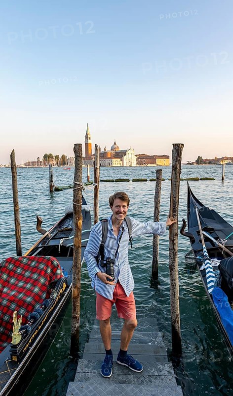 Young man at a boat dock for Venetian gondolas in St. Mark's Square, tourist enjoying the evening, back church of San Giorgio Maggiore in the evening light, Venice, Veneto, Italy