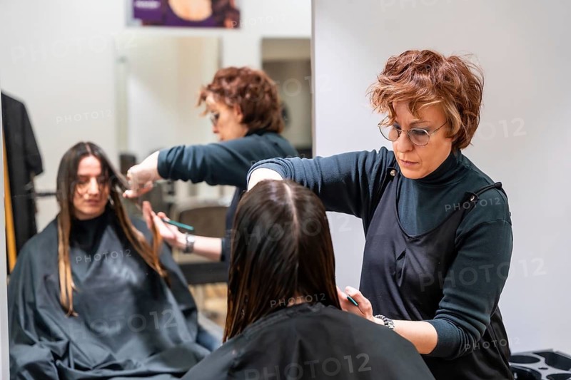 Stylist carefully trimming a young woman's hair in a modern hair salon, focusing on precision and technique during the haircut for beauty and grooming