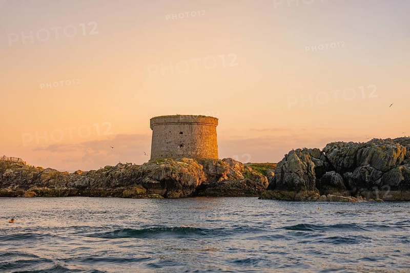 A historic tower rises on rocks along the coast at sunset, Howth, Ireland