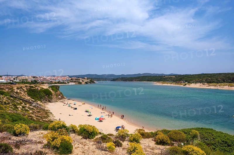 Sunny beach day with people under umbrellas along a wide sandy beach on a coast, Vila Nova de Milfontes, Beja, Portugal
