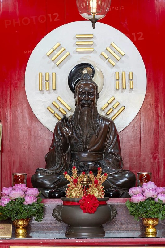 A dark, intricately crafted statue of Laozi (Lao Tzu), the legendary philosopher and founder of Daoism, set against a large Yin-Yang symbol and surrounded by the eight Bagua symbols. Red panels with golden characters and offerings, Chee Chin Khor Temple, Bangkok, Thailand