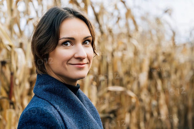 Portrait of attractive young woman in autumn coat in cornfield