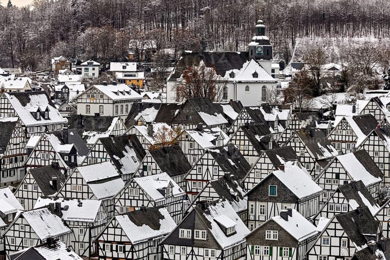 Snow-covered half-timbered houses and a church in a village in front of a wooded hill, The historic half-timbered houses from Alter Flecken in Freudenberg