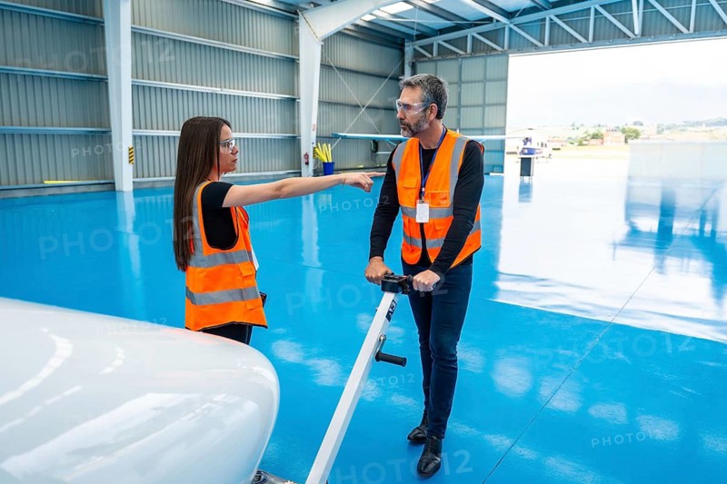Aviation professionals wearing safety vests and goggles collaborating and communicating inside an airplane hangar, preparing aircraft for operations and demonstrating teamwork and maintenance