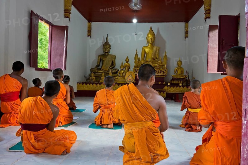 Laotian novices in orange robes in front of a golden Buddha figure in a newly built Buddhist monastery in the village of Muang Ngoi on the Nam Ou River, Phongsali province. laos