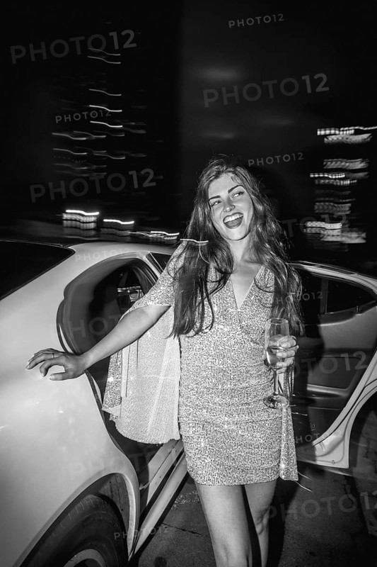 Young elegant woman in a shimmering sequin dress holding a champagne glass, stepping out of a limousine, celebrating a special event during a glamorous night out