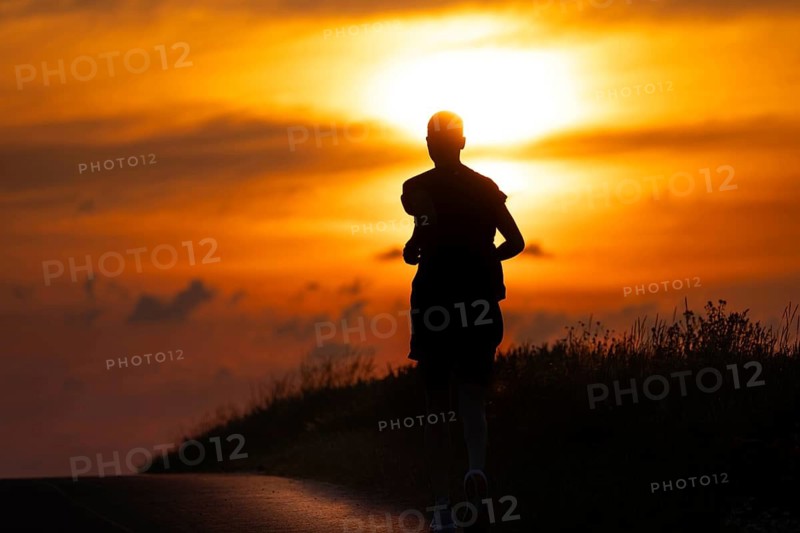 A female jogger runs along a Feldberg near Frankfurt am Main in the morning just after sunrise, Frankfurt am Main, Hesse, Germany