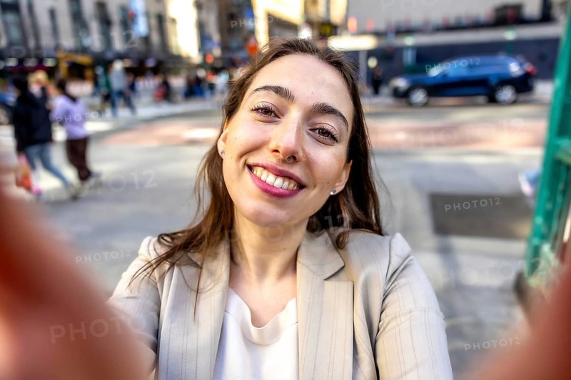 Young woman smiling into the camera for a selfie while exploring manhattan, capturing a joyful, candid moment of urban life and travel in warm daylight streetscape
