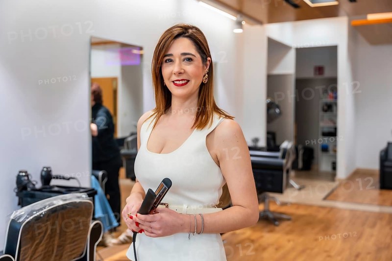 Professional hairdresser in a salon holding a flat iron, smiling confidently while preparing to style a client's hair, showcasing cosmetology expertise and modern beauty service
